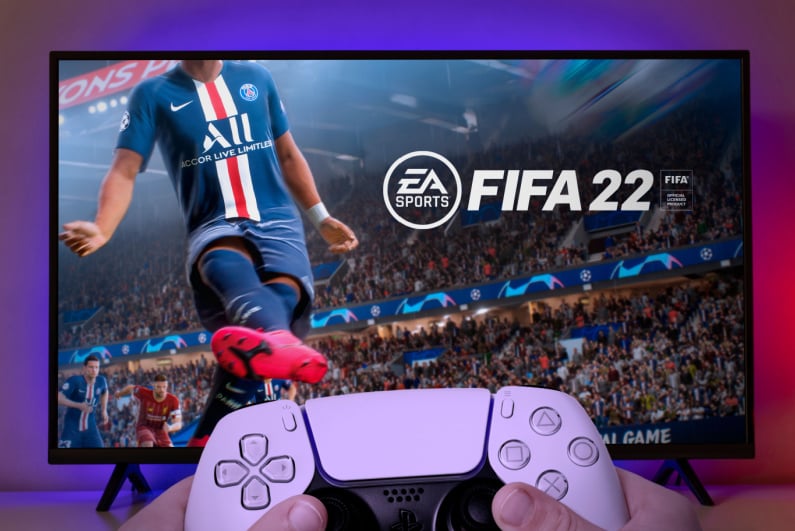Person holding a PlayStation controller with FIFA 2022 on the TV