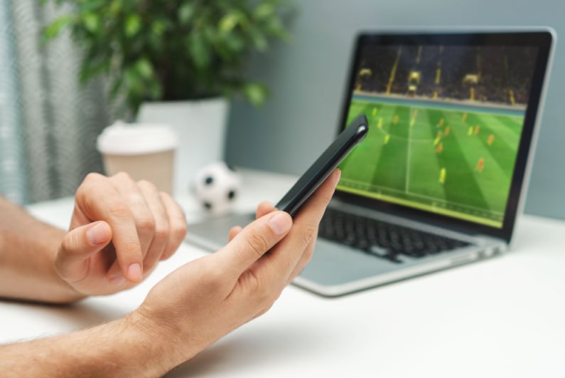 Person looking at phone with soccer on laptop