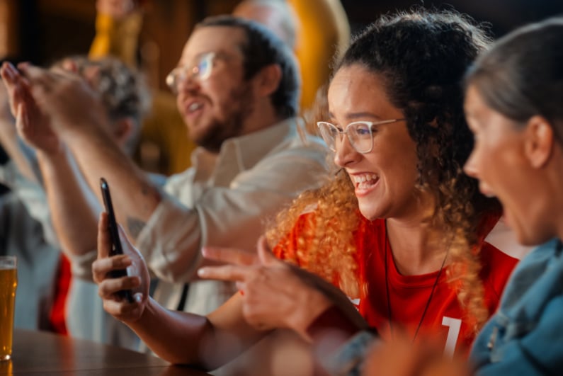 Two women at a sports bar excited about a bet on a phone